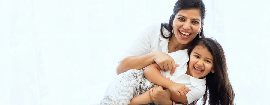 A mother and her young daughter laugh and hug each other's on a couch