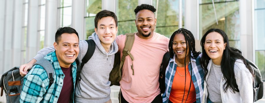 Cheerful group of diverse students standing outside a modern educational building on a sunny day.