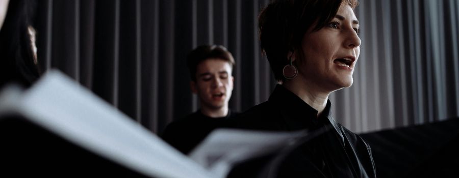 Two individuals, a man and a woman, singing as part of a bigger choir