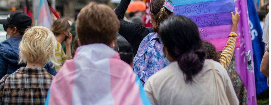 People walking during a protest in support of trans rights, one individual wearing a trans flag around their shoulder