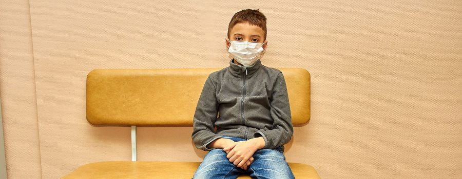 Young boy wearing a face mask sits on a bench, highlighting the new normal in healthcare settings