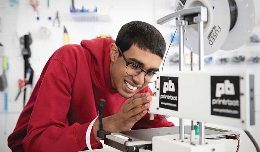 A student smiling while using a 3D printer.