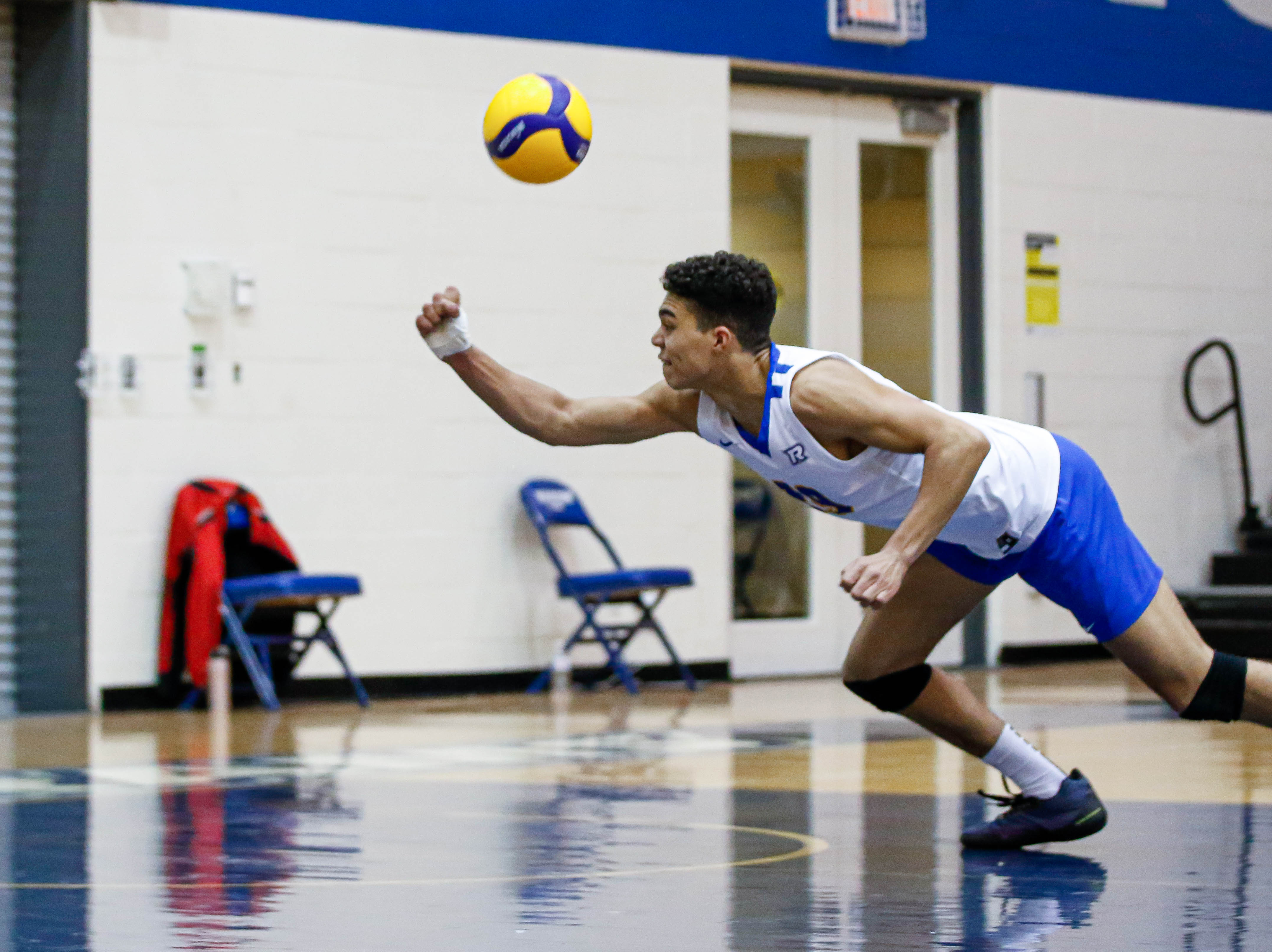 A volleyball player lunges with an outstretched fist attempting to bump a volleyball