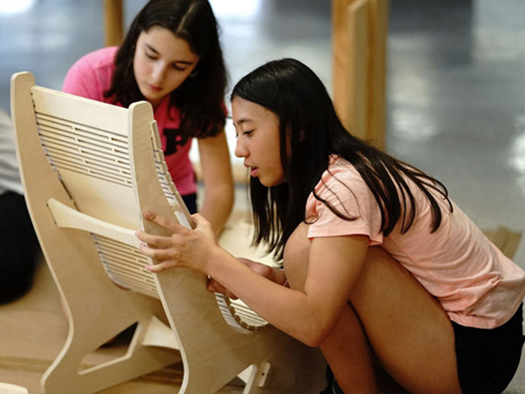 Two youth are working with their hands to assemble a wooden chair