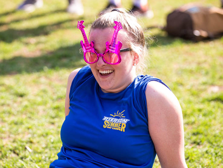 A camp staff sits in the quad wearing funny glasses