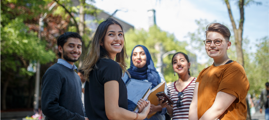 A group of five students standing together on a tree-lined street.