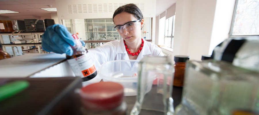 Female chemical engineering student in a lab looking at a bottle she is holding.