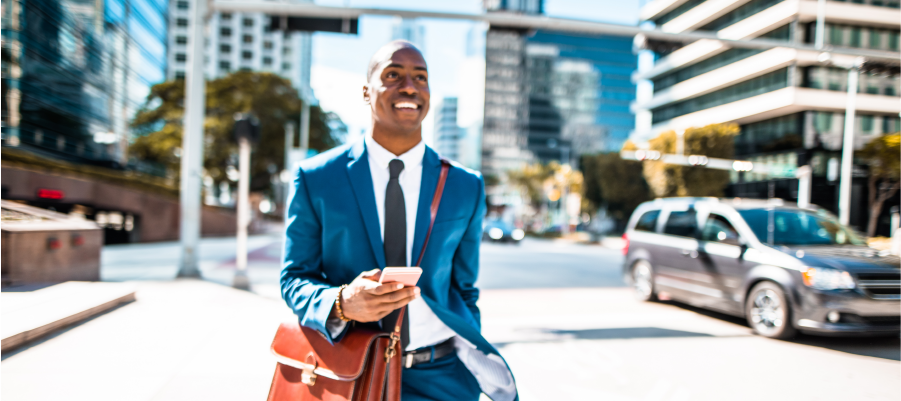 Man in suit with a briefcase over his shoulder and a phone in his hand walks down the street.