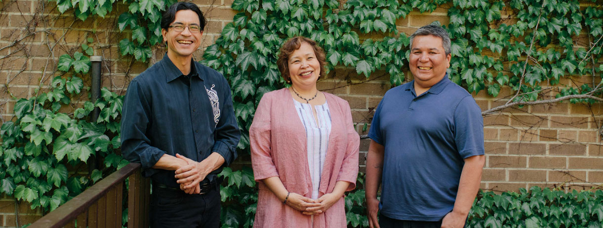 Three Indigenous employees smiling for a group photo outside TMU's Kerr Hall.