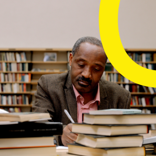 A man sitting next to a stack of books in a library.
