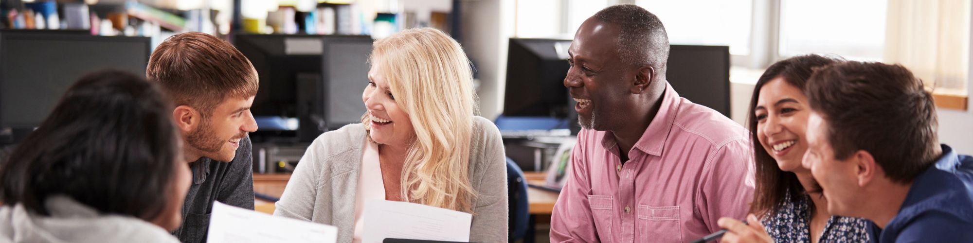 A diverse group of educators smile while in discussion in a library. 