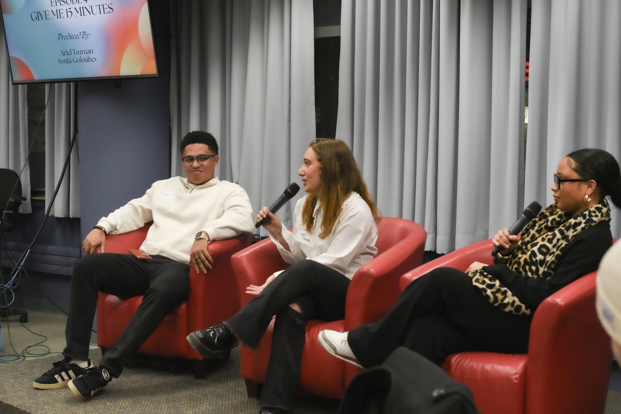 Three student producers sit, holding microphones and answering questions at the Season 4 listening party. 