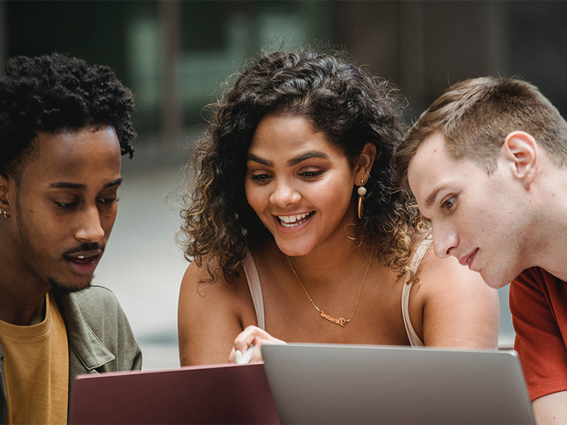 Three people leaning sitting around a laptop.