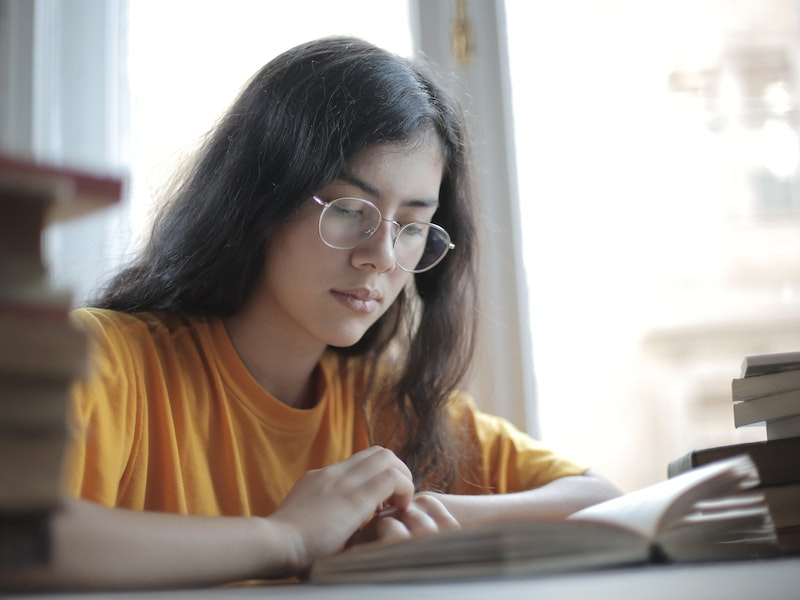 A student with long brown hair and glasses reading a book