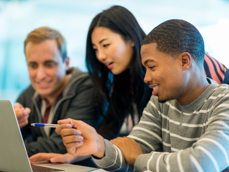 Three people gesturing towards a laptop screen with interest and enthusiasm.