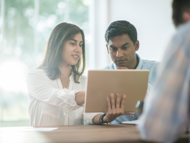 Person pointing to a laptop screen while another person looks on.