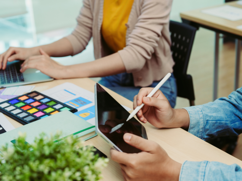 Two individuals sitting at a desk with their tablets and laptops.