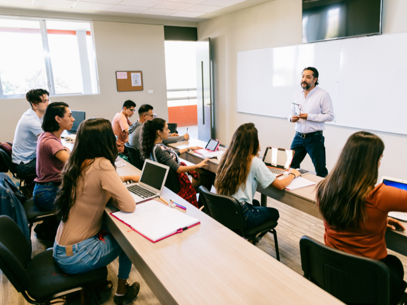 Lecturer standing and speaking at the front of a class.
