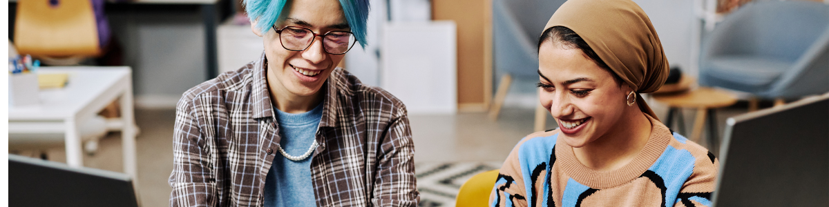 A student sits at a laptop, sharing something with their professor who sits next to them.