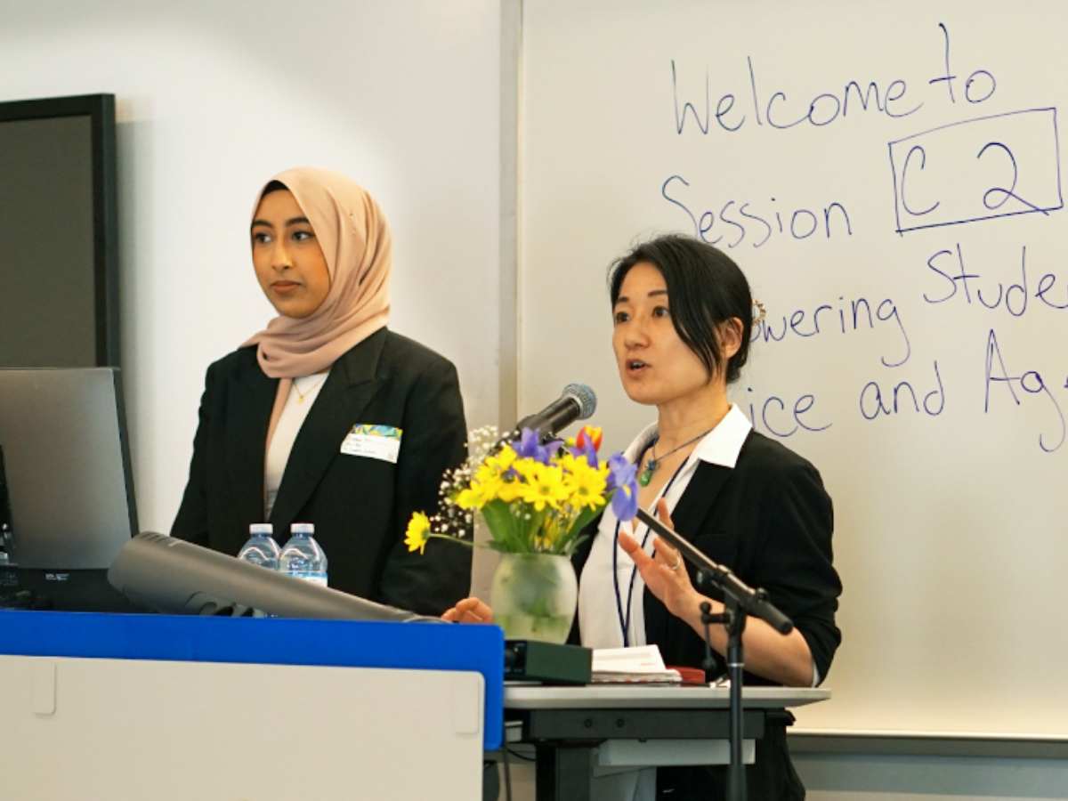 Professor gives a presentation with a colleague, standing at a podium