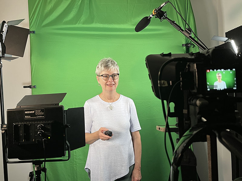 A person standing in front of a green smiling smiling while looking into the lens of a camera