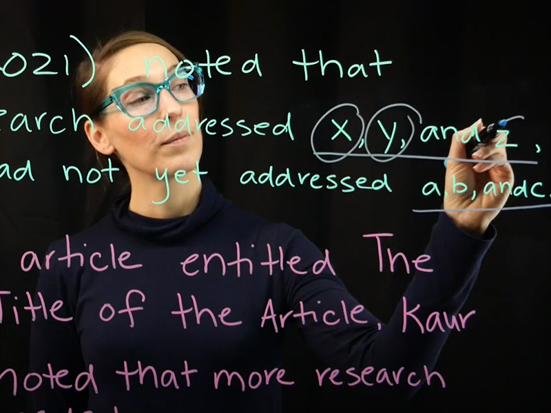 A person standing behind a clear whiteboard with text written in multicoloured marker