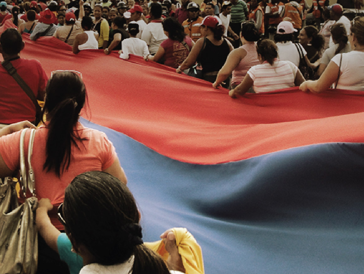 Crowd carrying a large flag of Venezuela down a street