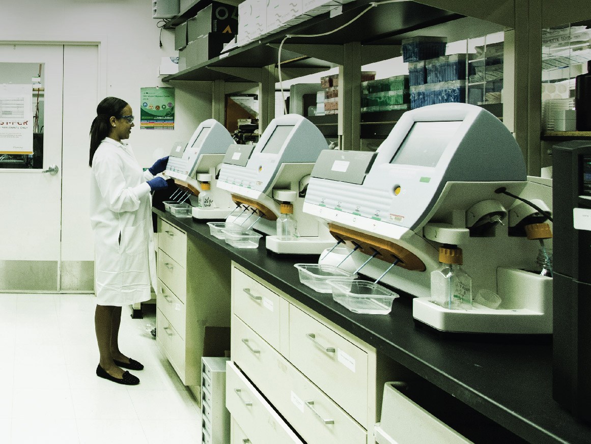 A technician works in a lab in front of a desktop genomic sequencing machines
