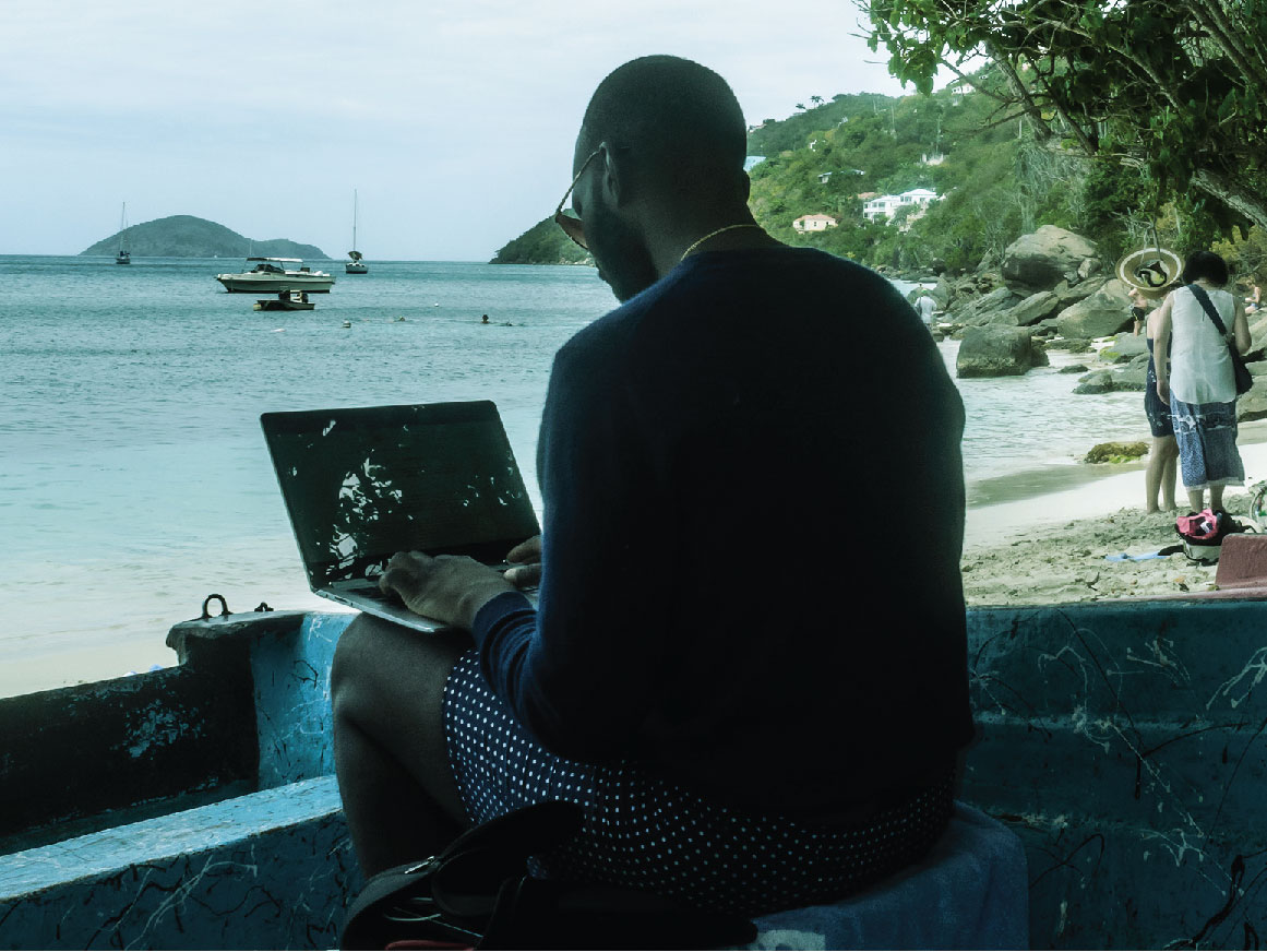 Man on a beach working on his laptop