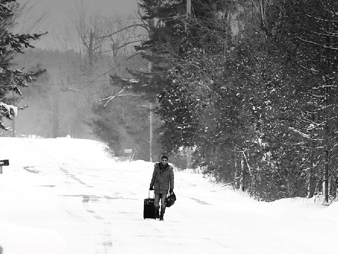 Man walking with a suitcase in the snow at Roxham road