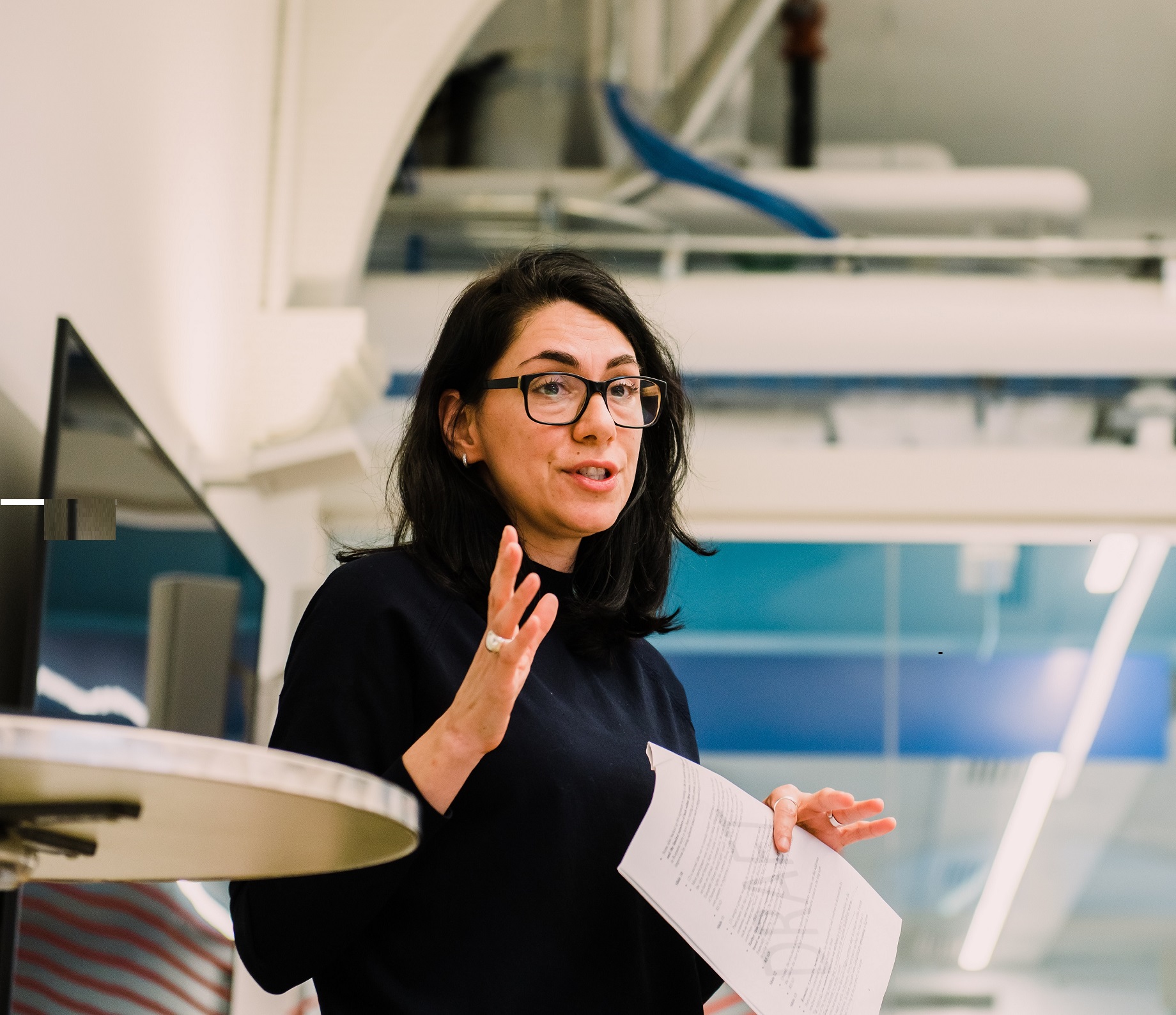 Woman with glasses speaking holding a piece of paper 