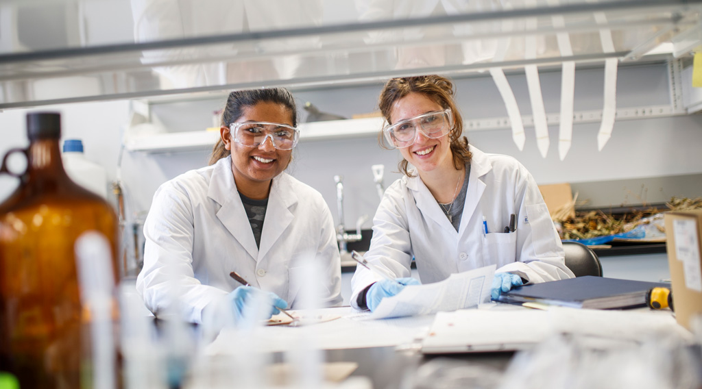 Chemistry and Biology undergraduate students smiling while working in the lab.