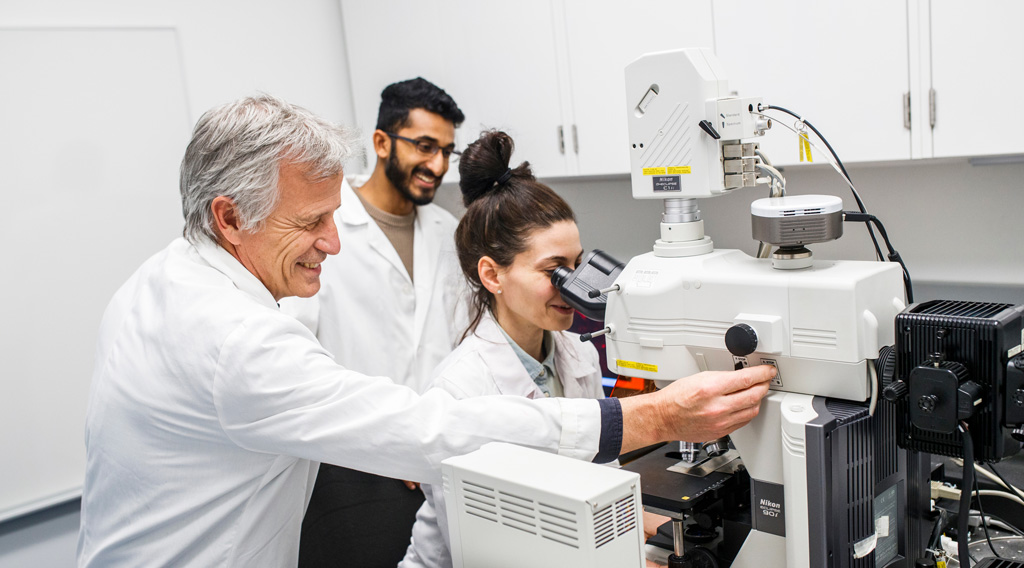 Chemistry and Biology graduate students working in the lab on a powerful microscope with their professor.