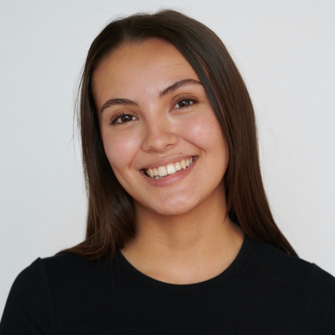 Smiling woman with long, straight hair wearing a black top against a plain white background. She conveys warmth and friendliness.