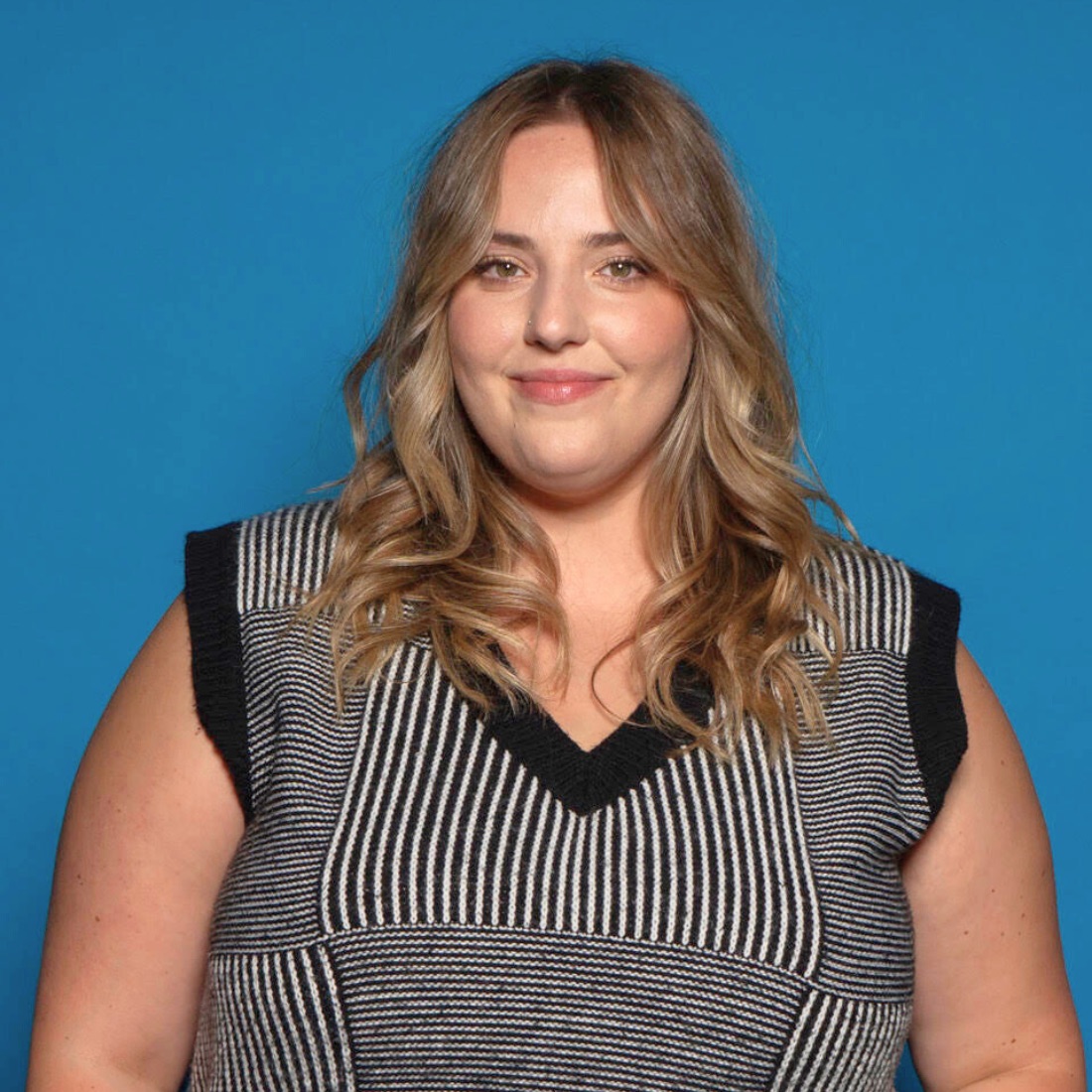 Smiling woman with wavy blonde hair in a black and white striped top against a solid blue background
