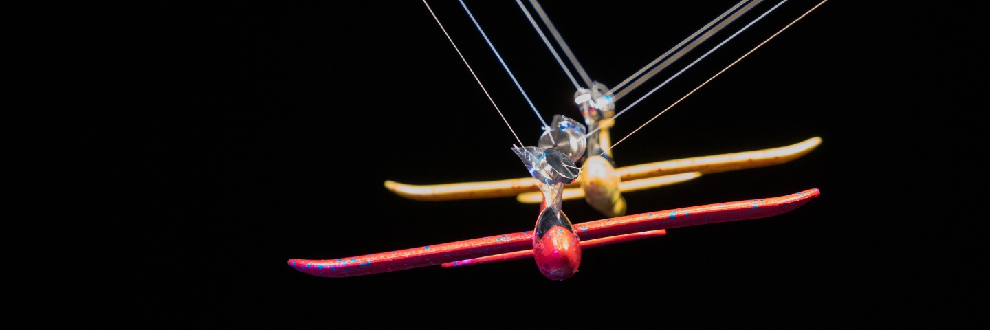 A red and a yellow glass airplane model suspended with strings against a dark background.