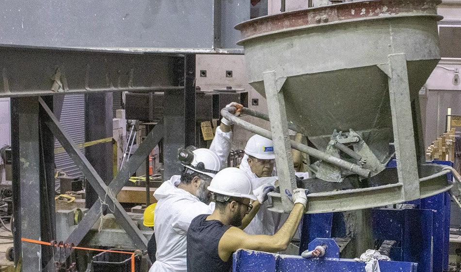 A group of researchers in a lab maneuver a large device that pours wet concrete into a cast