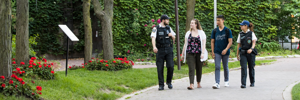 Two members of the security team smiling and walking with students in the Quad.