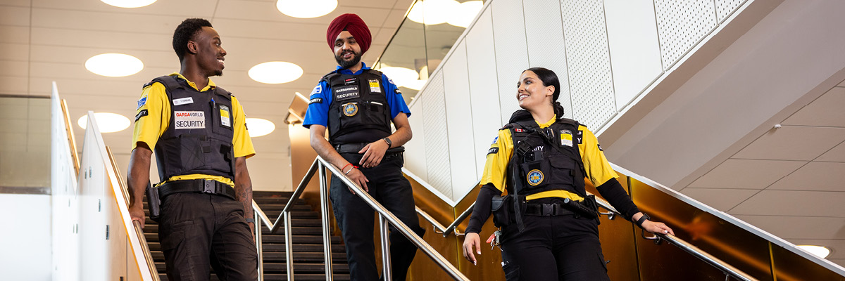 Three TMU Security staff walk down the stairs in the DCC, smiling and talking to each other.