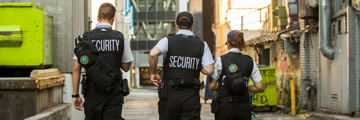 Three members of the security team walking in an alley. The word SECURITY is written on their backs.