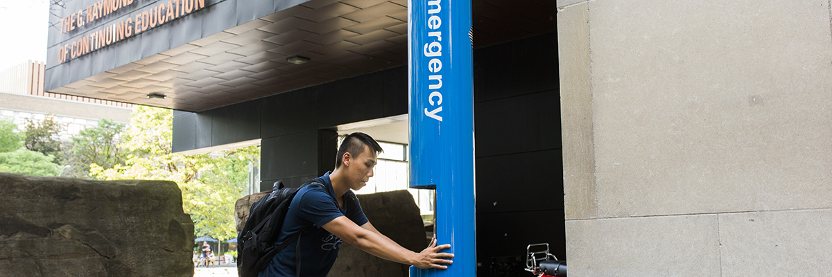 A person making a call using one of the blue emergency polls on campus.