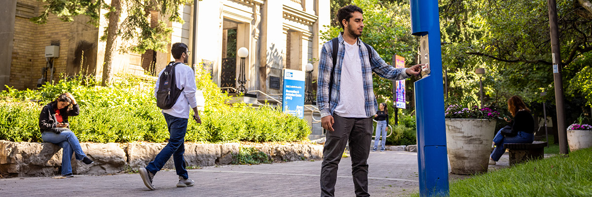 A student pushes the button on a blue emergency pole in the Quad to contact TMU Security for help.