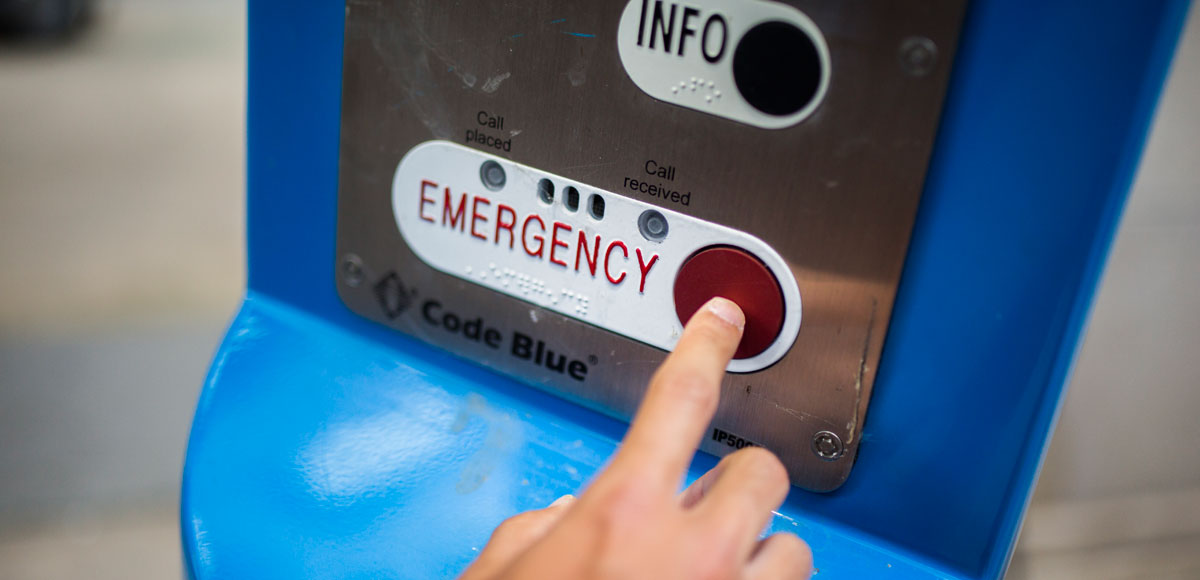 A hand pressing the red emergency button at an emergency station on campus.