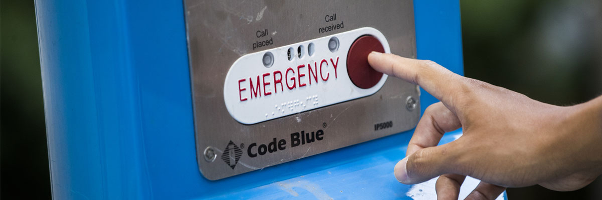 A hand pressing the red button on one of the emergency stations on campus.