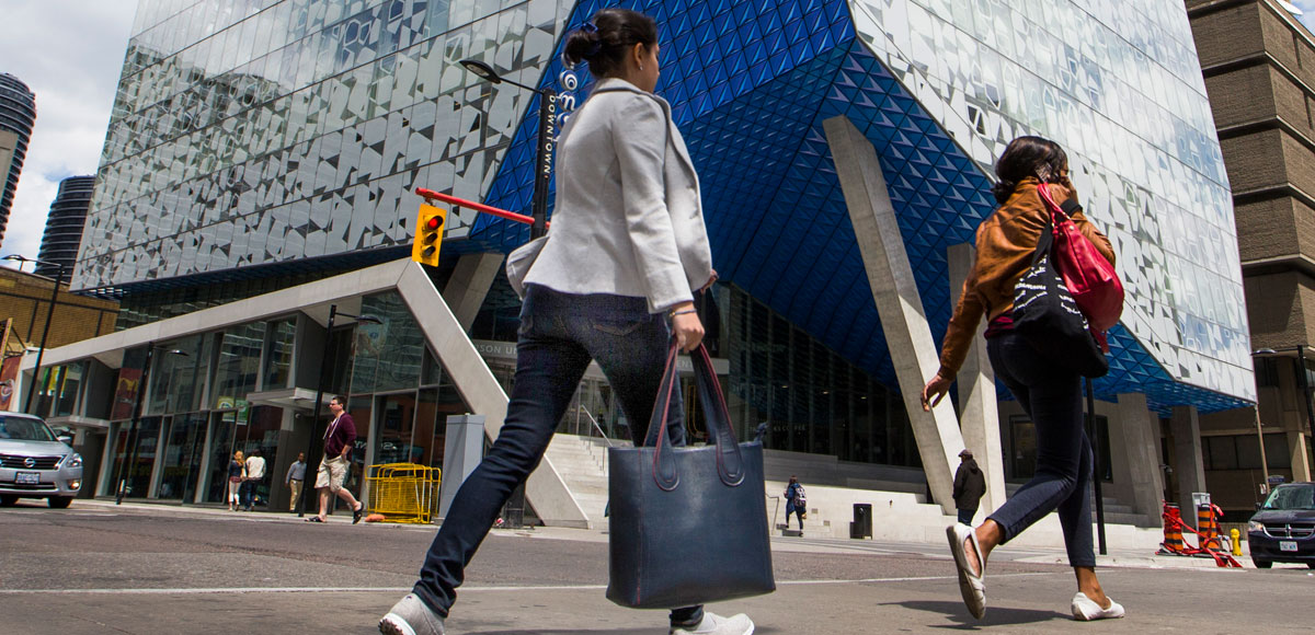 Person carrying leather bag crossing the street in front of the SLC.