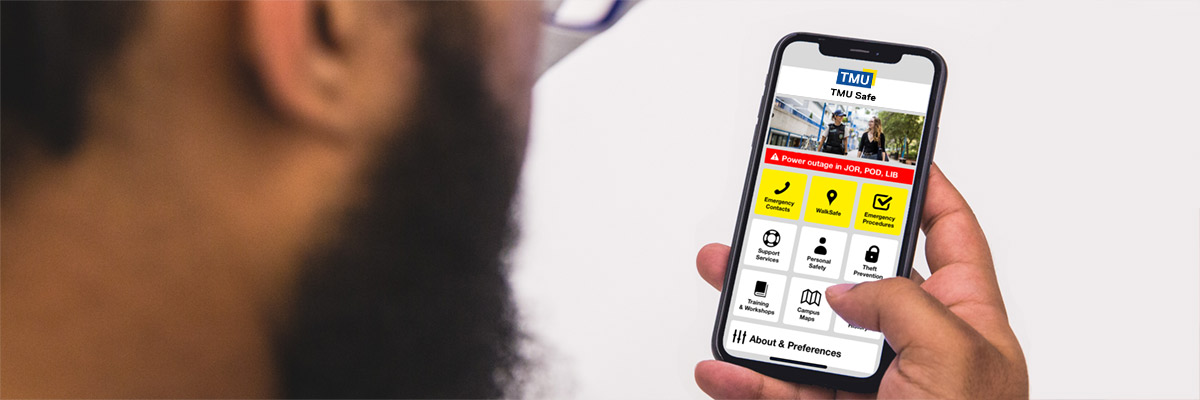 A TMU communication member looking at the TMU Safe mobile app on their smartphone.