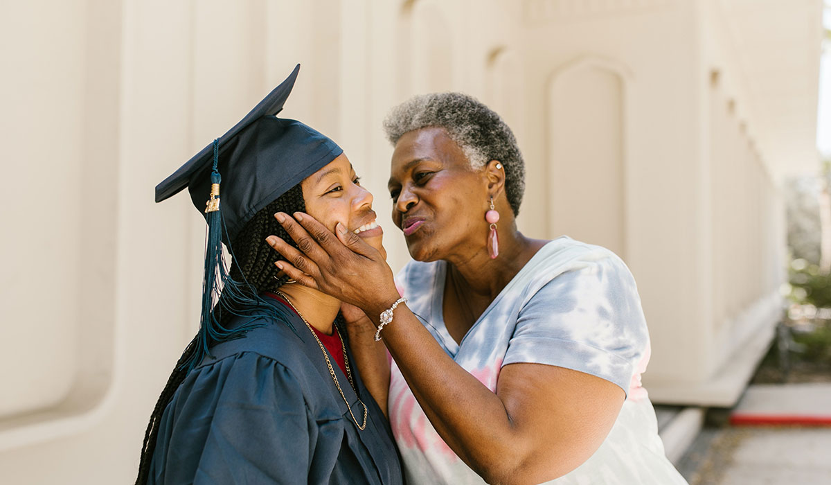 Black graduating student being warmly embraced by an elder.