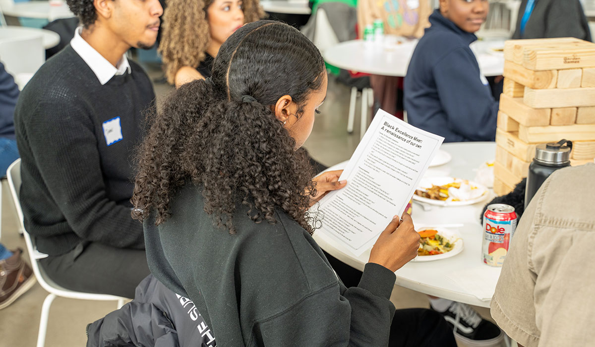 Black student at the Black Excellence Mixer reading a guide sheet. 