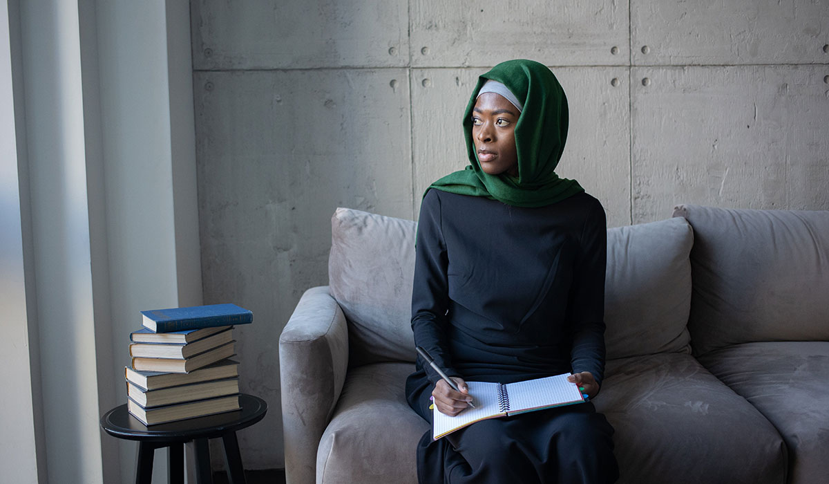 Black woman in a headscarf deep in thought and writing on a notepad. 