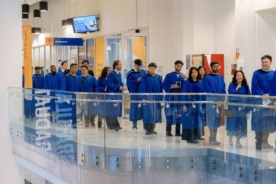 A group of graduands dressed in blue Bachelor's gowns are lined up for the graduand procession outside the Varsity Court 